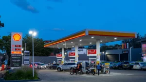 a-busy-shell-fuel-station-in-the-evening-with-customers-on-the-forecourt-cars-and-motorcycles-refueling-and-a-convenience-store